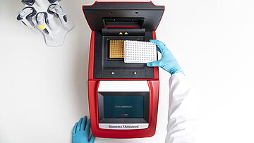 Overhead view of a scientist placing a 96-well plate into a Biometra T-advanced thermal cycler.