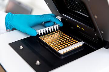 a gloved hand placing an 8-well PCR strip into the heating block of a qTOWER iris qPCR instrument